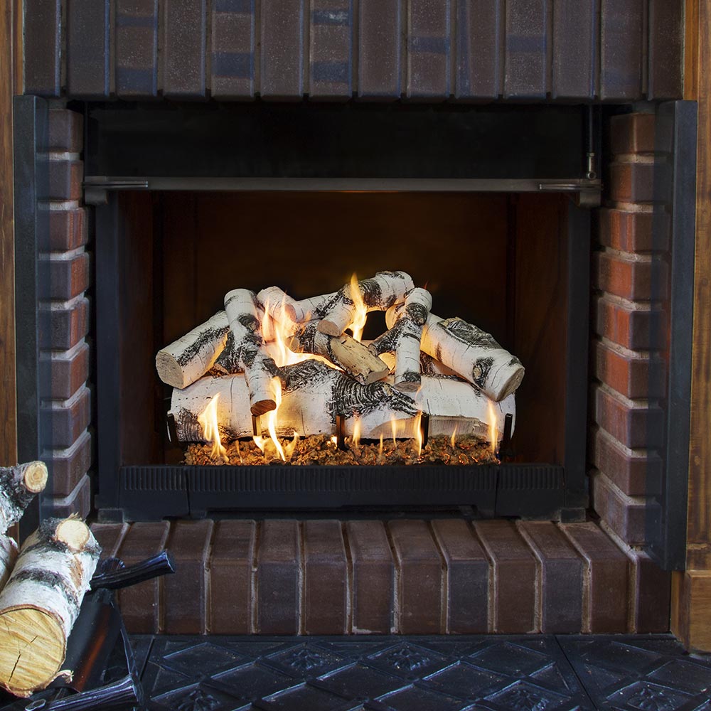 Vented gas log set in brick fireplace with flames and black firebox screen