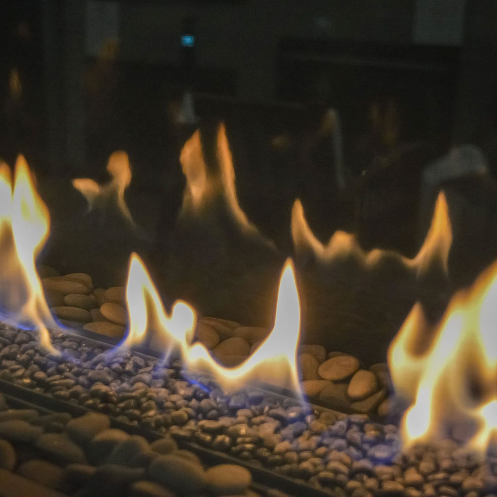 Built-in linear gas fireplace with glowing flames and dark fireglass rock media