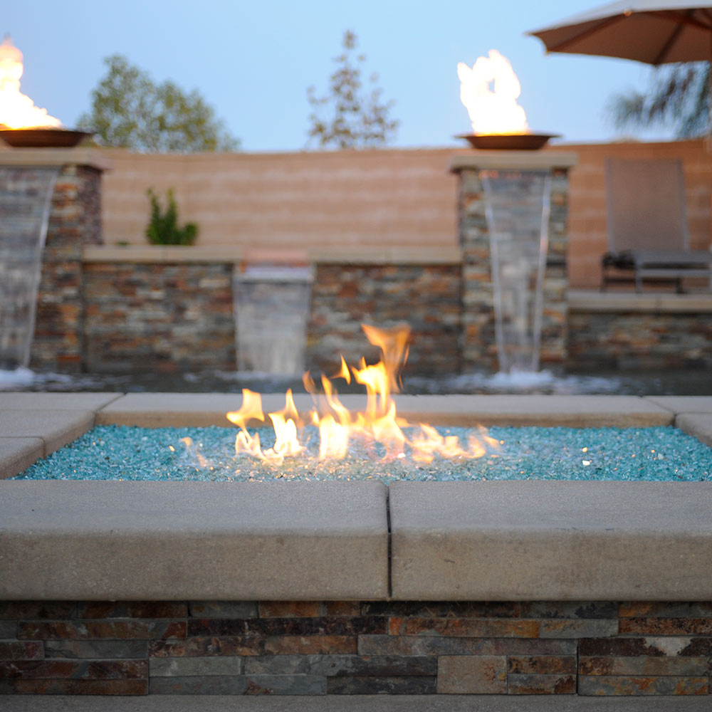 Outdoor fire pit with Azuria blue fire glass bed and visible flames