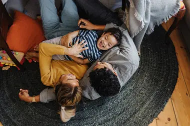 Top down photo of three family members laughing and playing on the floor