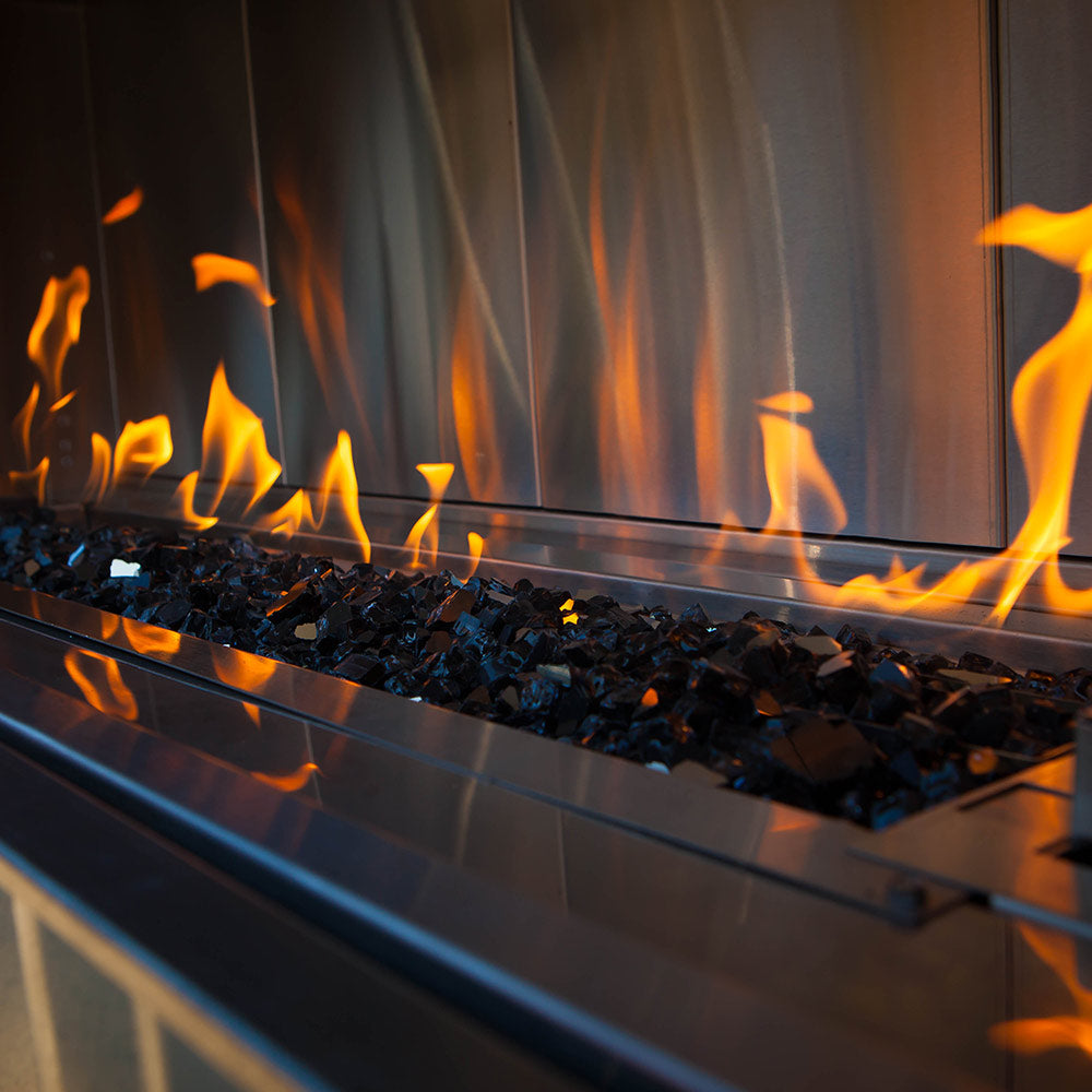 Blue broken fireglass pieces in a burner tray with flames rising in front.