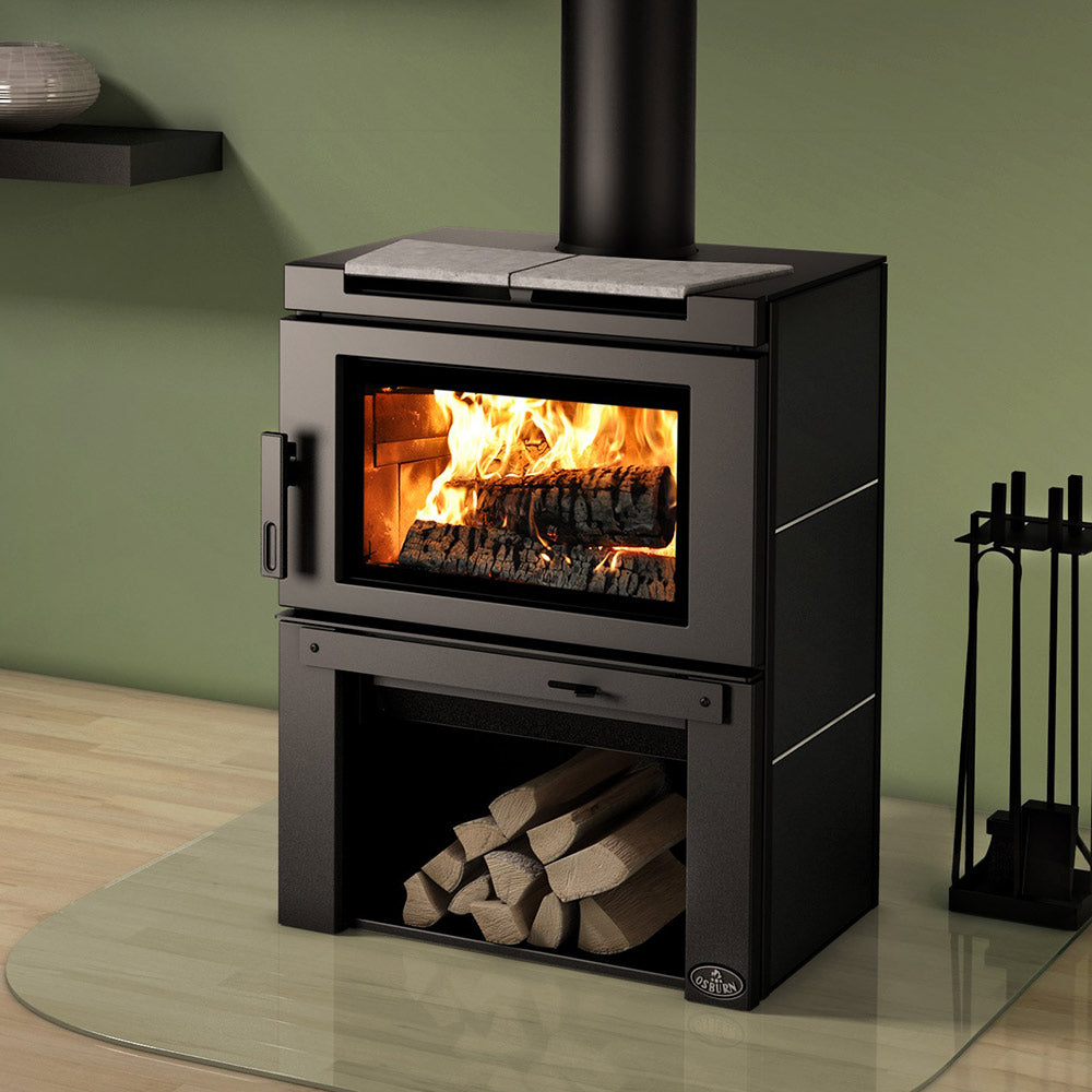 Wood stove with glass door, flames, and light stone top panel over log storage