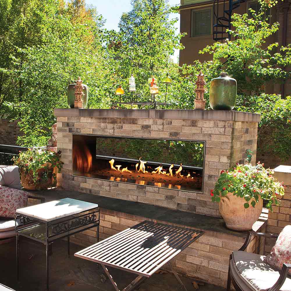 Outdoor linear fireplace with see-through flame window in a stone surround