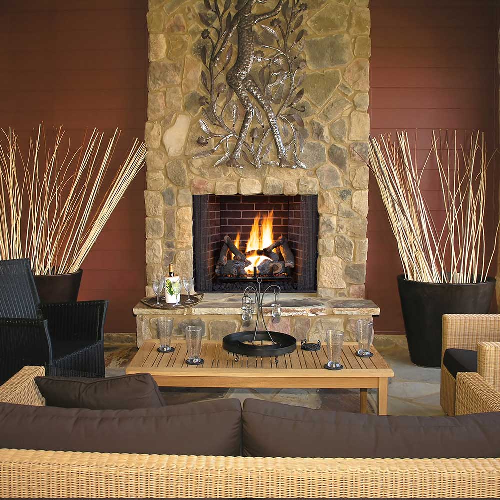 Gas log set with charred ceramic logs and active flames in a stone fireplace surround.