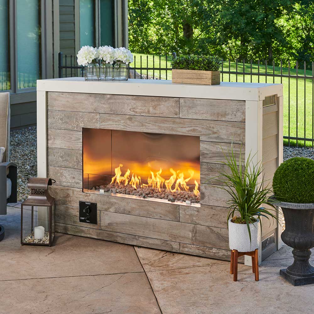 Outdoor linear single-sided fireplace with stone-look surround and glass viewing, flames burning