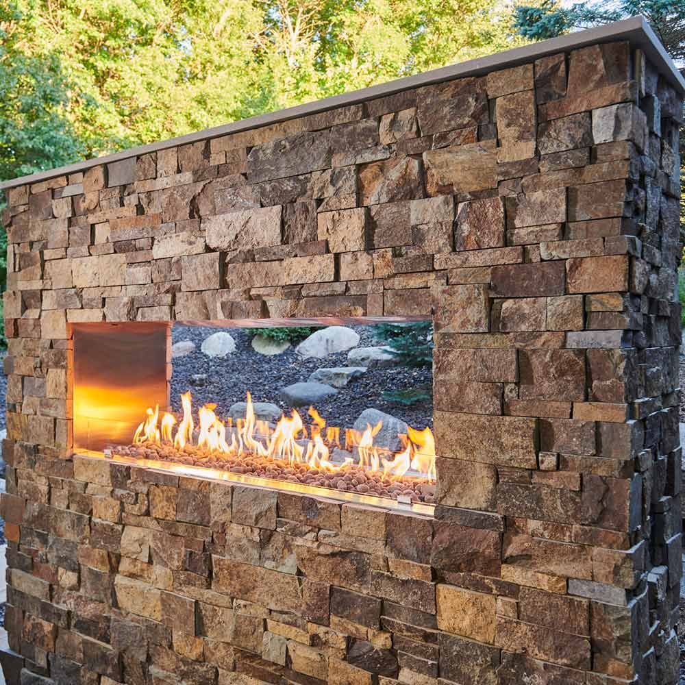 Stone-surround linear see-through fireplace with glass viewing window and burning flames