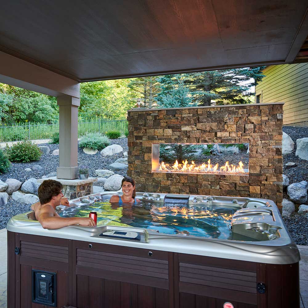 Outdoor linear see-through fireplace set into stone wall, glass viewing window with flames