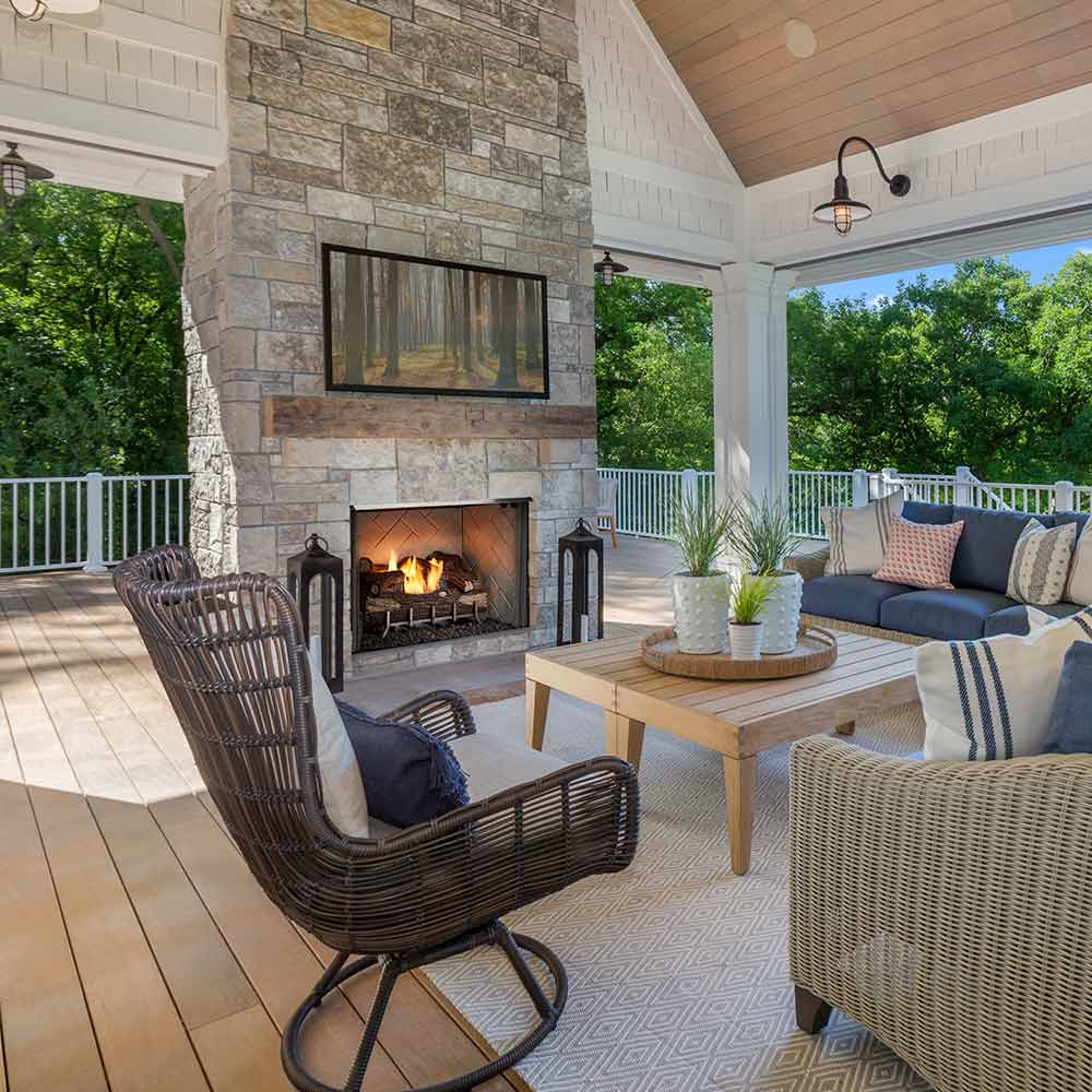 Outdoor gas fireplace insert in stone surround with burning logs and black mesh safety screen