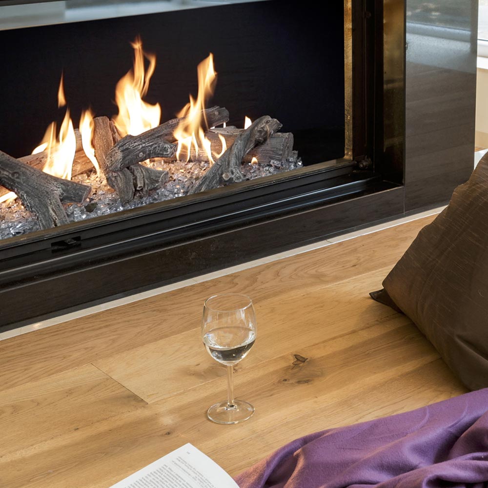 Linear gas fireplace with burning logs seen through clear glass panel