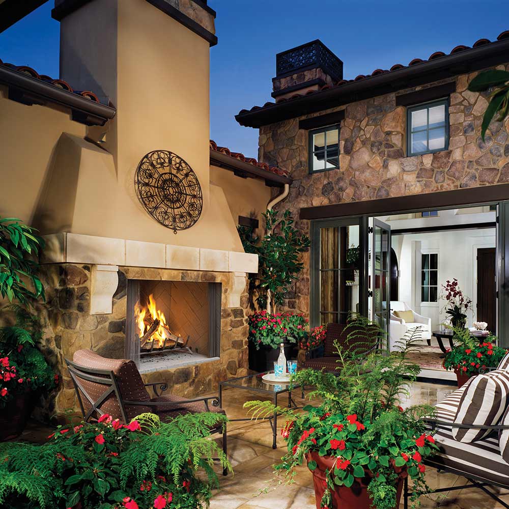 Outdoor wood burning fireplace set into stone wall with glass door and burning wood