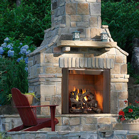 Outdoor wood fireplace with stone surround, open front, burning logs and twin side lamps