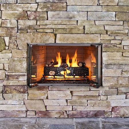 Outdoor gas firebox with glass doors and burning log set set into stone surround